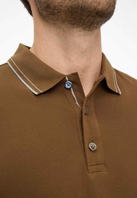 Polo marrone con un tessuto strutturato. Presenta una striscia grigia a contrasto sul colletto e bottoni blu e marroni sul collo.