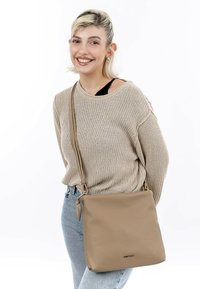 Beige Leder Umhängetasche mit glatter Textur, quadratischer Form und verstellbarem Trageriemen. Verfügt über ein dezentes Logo-Detail in der Nähe des Bodens.