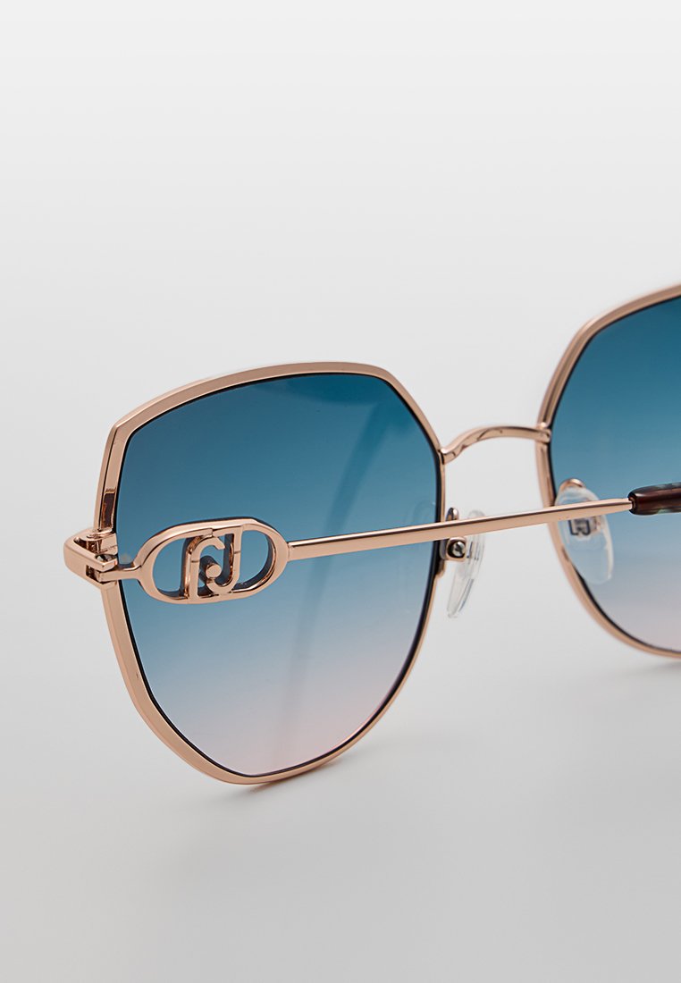 Hexagonale zonnebril met een roségouden metalen frame, blauwe ombre lenzen, zilveren logoaccent aan de zijkant en doorzichtige neuskussentjes.