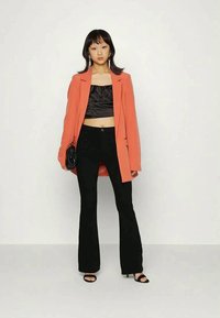 Blazer oversize em coral, top cropped de satém preto, calças flare pretas e sandálias de salto aberto. Mala preta simples, cabelo de comprimento médio, textura lisa.