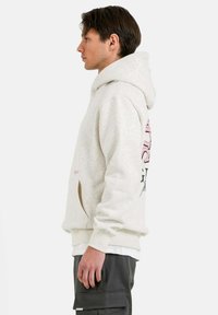 Lichtgrijze hoodie met een ruime capuchon, buidelzak en een roze grafische print op de achterkant. Zacht materiaal, geribbelde manchetten en onderrand.