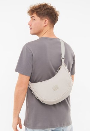 Graue Schultertasche mit geschwungenem Design, aus weichem Stoff gefertigt. Verfügt über einen einfachen Trageriemen und ein kleines Etikett auf der Vorderseite. Geeignet für den alltäglichen Gebrauch.