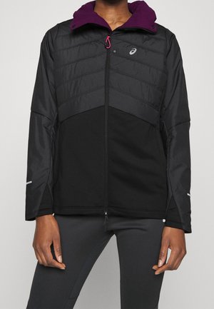 Man draagt een zwarte en donkergrijze jas met rits, met een paarse binnenkraag en een reflecterend logo op de borst en mouwen.