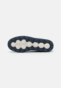 Schuhsohle mit einem kreisförmigen Muster, überwiegend marineblau mit weißen Akzenten. Eingebettete Textur für Traktion und Flexibilität.