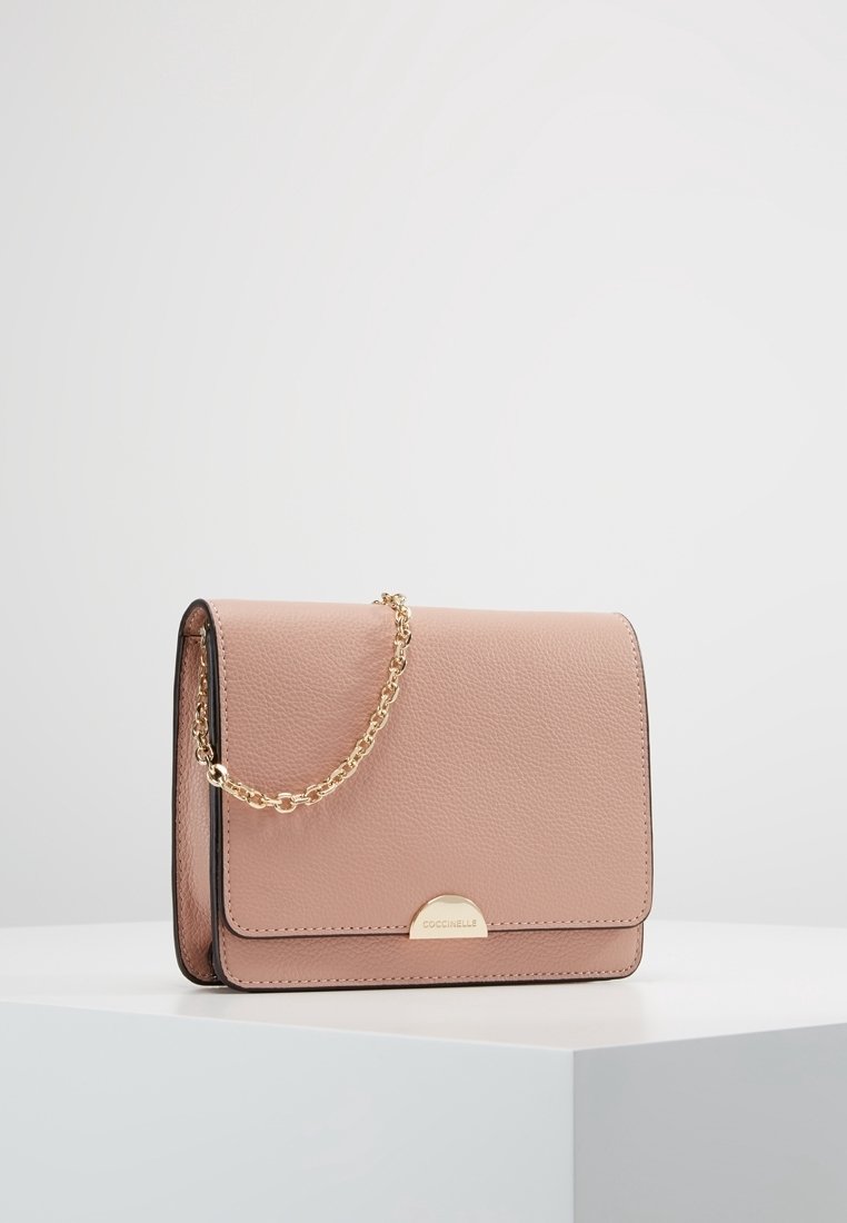 Rosa läderhandväska med en slät yta, guldkedjeaxelrem och en rund metallklämma. Har en enkel rektangulär form och rena kanter.