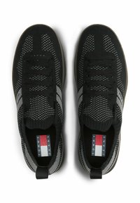 Schwarze gestrickte Sneakers mit grauen Akzenten, ausgestattet mit einem strukturierten Obermaterial, Schnürsenkeln und einer Zuglasche. Das Logoschild im Inneren zeigt die Markeninformationen.