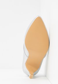 Chaussure à talons hauts en cuir argenté avec un bout pointu. Dessus lisse, semelle en caoutchouc beige clair avec une texture antidérapante, dotée d'une petite languette de talon.