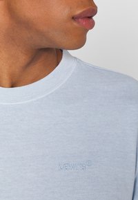 Světle modré bavlněné tričko s kulatým výstřihem. Obsahuje vyšívané logo Levi's v trochu tmavší modré. Hladká textura, casual design.