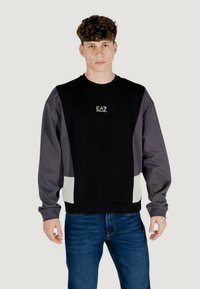 Felpa nera e grigio con tessuto testurizzato; presenta logo sul petto, pannelli a contrasto e polsini a costine; abbinata a jeans blu.