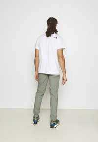 Biała bawełniana koszulka z małym czarnym logo z tyłu, w połączeniu z jasnobeżowymi spodniami i wielokolorowymi sneakersami z grubą podeszwą.