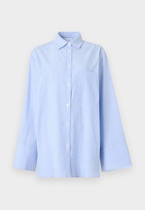 Lyseblå skjorte med knappestolpe, subtile vertikale striper, lange ermer, brede mansjetter og brystlomme på ensfarget bakgrunn.