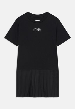 Melna T-kreka ar īsām piedurknēm un apaļu kakla izgriezumu. Tai ir plīšoša apakšējā daļa un neliels grafisks attēls augšējā priekšpusē.