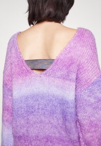 Lila und lavendel Farbverlauf Pullover mit tiefem V-Ausschnitt am Rücken, ausgestattet mit einem metallischen Riemen im Rückenbereich zur Unterstützung. Weiche Textur.