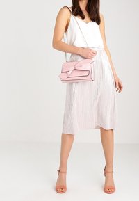 Jasnoróżowa torebka z akcentem w postaci kokardy, wykonana z gładkiego materiału. Połączona z satynową białą bluzką i błyszczącej, plisowanej srebrnej spódnicy.