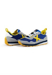 Baskets bleues et grises avec une touche de jaune, en haut texturé, à lacets et avec une semelle en caoutchouc au motif de traction distinct.