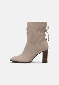 Bottines en suède beige avec un design flou, bout pointu et un talon empilé de 7,5 cm ; présente un accent avec cordon au sommet.