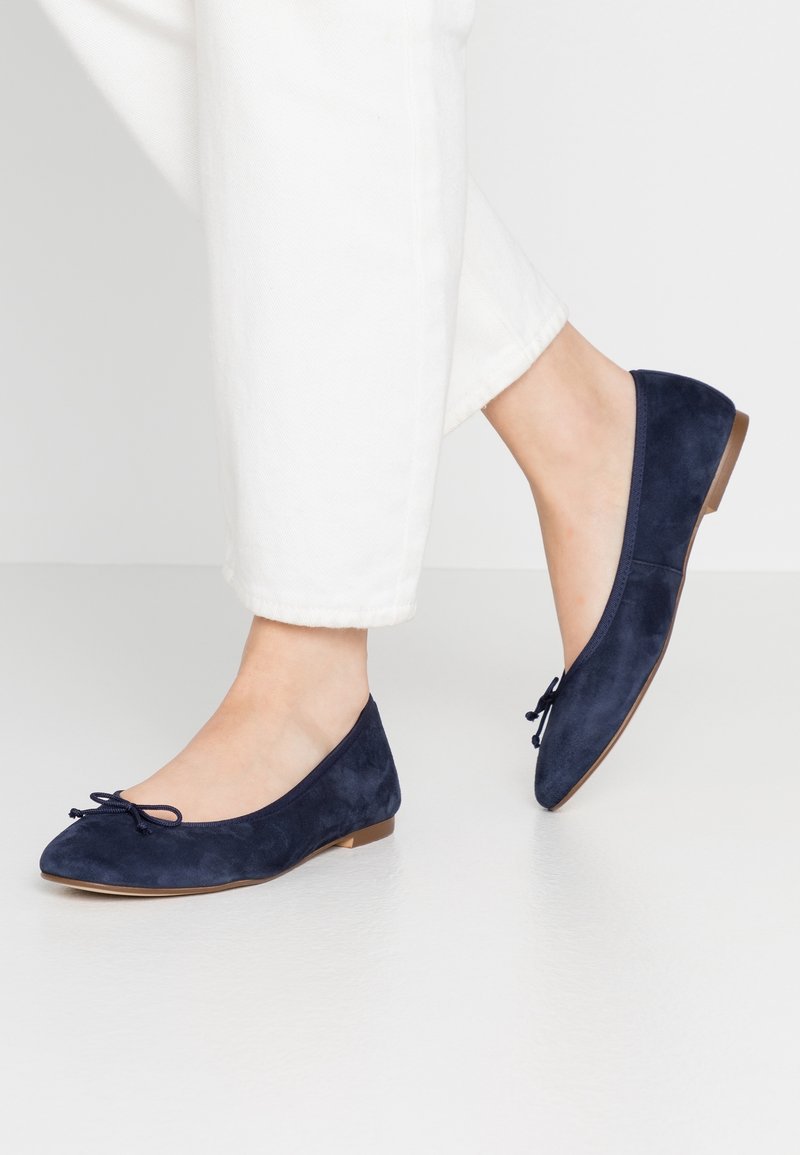 Ballerines en suède bleu marine avec un bout rond et un détail de nœud décoratif. Semelle plate avec une hauteur de talon minimale, texture lisse.