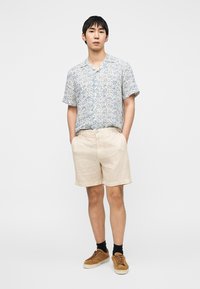 Chemise à manches courtes, bleu clair avec un motif, col classique, associée à un short beige et des baskets marron. La tenue présente une coupe décontractée.