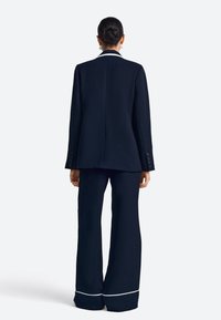 Conjunto de traje azul marino que incluye una americana entallada con un detalle de cuello blanco y pantalones de pierna ancha con un dobladillo blanco. Textura de tela suave.