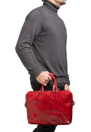 Valigetta in pelle rossa con finitura lucida, maniglie doppie e chiusura con cerniera, tenuta da una persona che indossa un maglione a collo alto grigio.