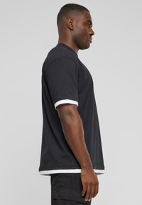 Sort bomulds T-shirt med hvide kontrast manchetter, afslappet pasform og rund halsudskæring, vist på en mandlig model fra siden.