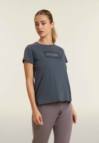 Camiseta gris de manga corta hecha de un tejido suave, con un diseño rectangular texturizado en la parte frontal. Cuello redondo, corte relajado.