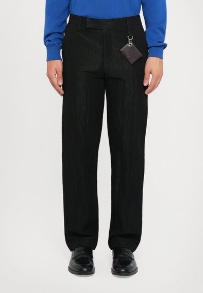 Pantalones negro texturizados con corte recto, que cuentan con un detalle de llavero en la cintura, combinados con zapatos negros y un suéter azul.