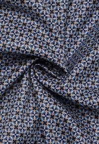 Stof met een geometrisch patroon met witte en lichtblauwe cirkels op een donkere marineblauwe en bruine achtergrond, met een zachte, gestructureerde afwerking.