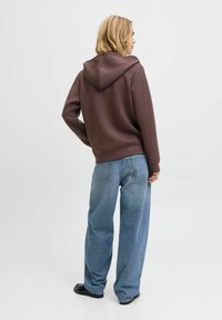 Felpa con cappuccio marrone realizzata in tessuto morbido, abbinata a jeans a gamba larga di un blu chiaro. Texture liscia e design semplice con una vestibilità comoda.