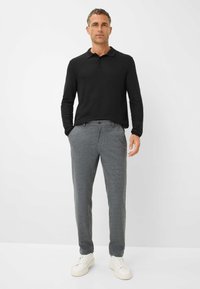 Polo noir à manches longues associé à un pantalon tapered gris. Tissu en mélange de coton, texture lisse et design minimaliste. Baskets blanches.