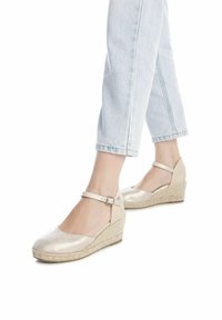 Zapatos de cuña beige con acabado metálico, correa al tobillo y suela de yute trenzado; textura suave con un diseño de parte trasera abierta.