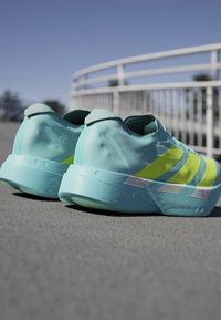 Turquoise running shoes featuring a textured surface, yellow accents, and a sleek design. Lightweight construction with a prominent midsole.