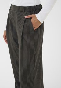 Donkere gestreepte broek van gladde stof met een elastische tailleband en zijzakken. Beschikt over subtiele krijtstrepen in verschillende kleuren.