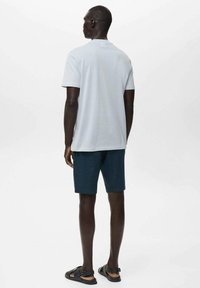 Light gray short-sleeve t-shirt, paired with dark blue shorts. The outfit features soft fabric and a relaxed fit, with black sandals.