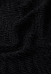 Tessuto nero testurizzato con un sottile motivo intrecciato, che mostra morbide pieghe e una superficie liscia. Colore principalmente profondo e uniforme.