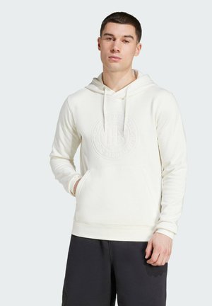 Helle Creme-Hoodie aus glattem Stoff, mit einer Vordertasche und einem geprägten Logodesign. Kombiniert mit dunklen Shorts.