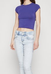 Lila Cropped T-Shirt aus glattem Baumwollmaterial, mit kurzen Ärmeln und rundem Ausschnitt, kombiniert mit hellblauen Skinny Jeans.