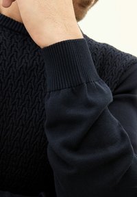 Dunkelblauer Pullover mit strukturiertem Muster am Körper und gerippten Bündchen, ausgestattet mit einer glatten Stoffoberfläche und einer körpernahen Passform.