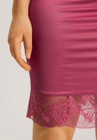 Vestido ceñido magenta con dobladillo de encaje transparente con patrones florales. La tela suave contrasta con la delicada textura del encaje.
