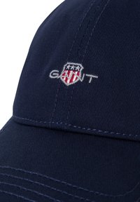 Gorra de béisbol azul marino de algodón con logotipo bordado que presenta rayas rojas y blancas y tres estrellas por encima de la palabra "GANT."