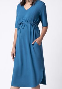 Niebieska sukienka do kolan, wykonana z miękkiego materiału, z dekoltem w kształcie litery V, krótkimi rękawami, elastyczną talią ze sznurkiem oraz bocznymi kieszeniami.