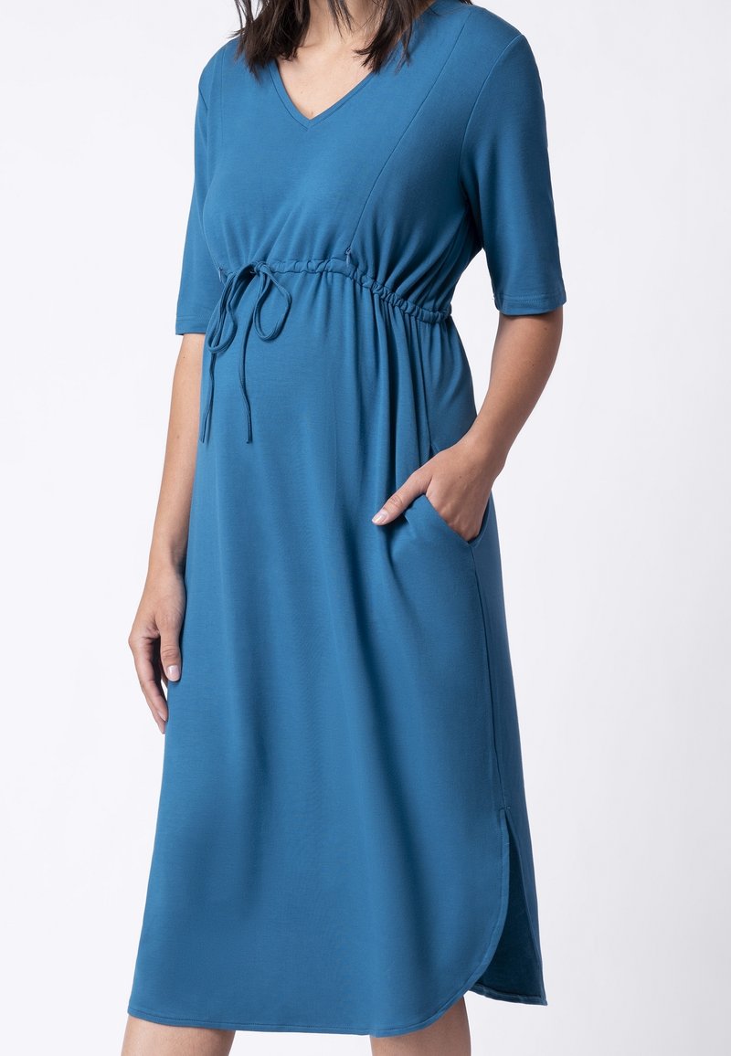 Niebieska sukienka do kolan, wykonana z miękkiego materiału, z dekoltem w kształcie litery V, krótkimi rękawami, elastyczną talią ze sznurkiem oraz bocznymi kieszeniami.
