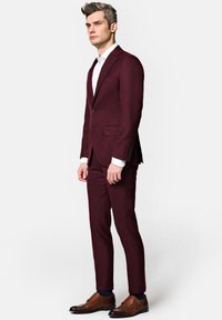 Bordowy garnitur o wąskim kroju, marynarka zapinana na jeden guzik, z klapami typu notch oraz kontrastową białą koszulą. Brązowe buty typu double monk strap dopełniają wygląd.