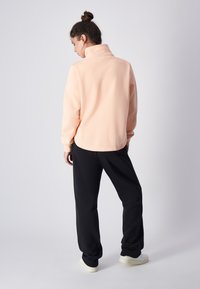Sudadera de felpa melocotón con cuello alto, combinada con joggers negros. Textura suave, corte relajado y puños acanalados, con un acabado liso.