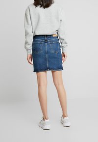 Gonna di jeans in lavaggio scuro con tasche posteriori, taglio dritto e orlo sopra le ginocchia, abbinata a una felpa grigia chiara e sneakers bianche.