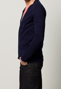 Cardigan blu navy realizzato in tessuto morbido, con scollatura a V, due tasche anteriori e chiusura a bottoni, abbinato a jeans scuri.