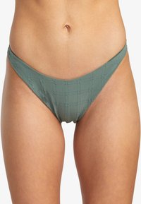 Grön bikiniunderdel i ett strukturerat tyg, med låg midja och minimal täckning. Mönster inkluderar diskreta upphöjda linjer.