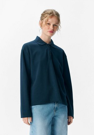 Polo de manga larga azul oscuro con cuello y tres botones, combinado con jeans azul claro. Diseño simple, textura suave.