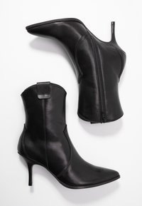 Stivali neri in pelle fino alla caviglia con punte affusolate, tacchi a stiletto, lati curvi e chiusura con zip. Presentano un accento a forma di anello sul retro.