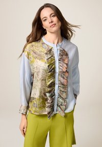 Camicia button-up con una parte anteriore multicolore decorata con rouches, tonalità di blu chiaro e verde, e righe verticali sulle maniche lunghe.